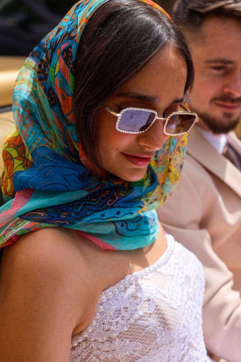 A bride in a colourful silk headscarf smiling in the sunshine
